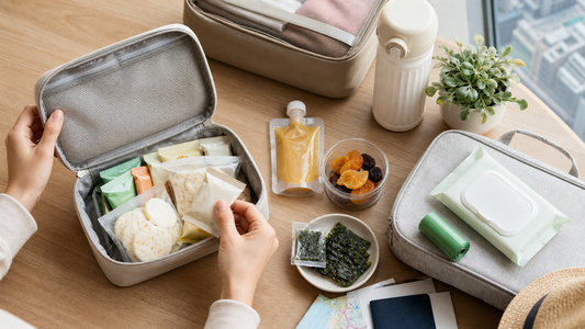 香港家長在窗邊桌上整理親子旅行零食包，內有無品牌獨立包裝米餅、果泥、果乾、海苔、濕紙巾和水樽